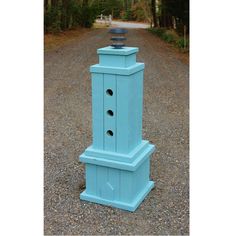 a blue tower sitting in the middle of a gravel road next to a wooded area