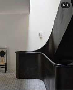 a black chair sitting in front of a white wall next to a wooden bench and tiled floor