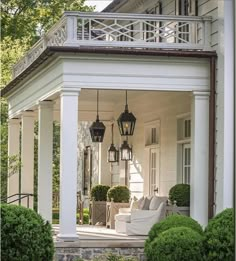 the front porch of a white house with two lamps on it's posts and bushes