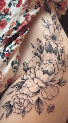 a woman's thigh with flowers and leaves tattoo on her side ribcage