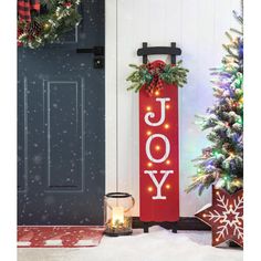 a red joy sign sitting in front of a door with christmas wreaths and lights