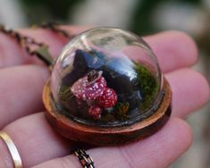 a tiny figurine in a glass ball on a chain is held by someone's hand