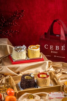 an assortment of desserts in wooden trays on a cloth covered tablecloth with red bag