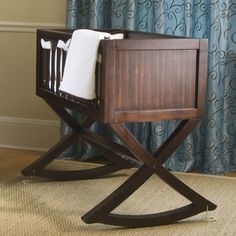 a baby crib sitting on top of a rug in front of a curtained window