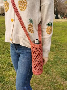 a woman is holding a crocheted pineapple bag in her hand while standing on the grass