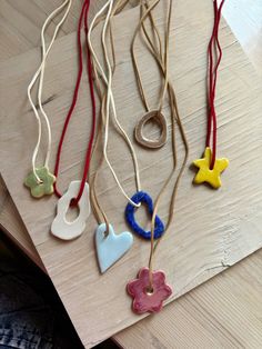 several necklaces with different shapes and colors hanging from strings on a wooden table top