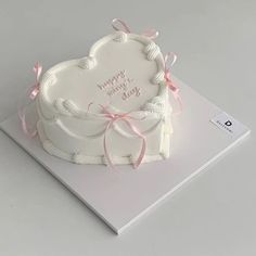 a white heart shaped cake with pink ribbon on it's side, sitting on top of a card