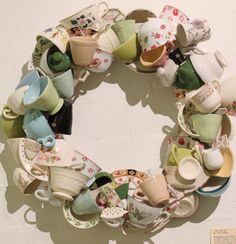 a wreath made out of tea cups and saucers on a white wall with a sign in the background