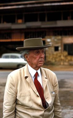 an old man wearing a suit and tie standing in the street with his hands on his hips