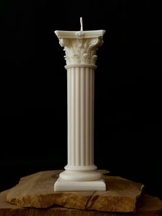 a tall white pillar sitting on top of a piece of wood next to a candle