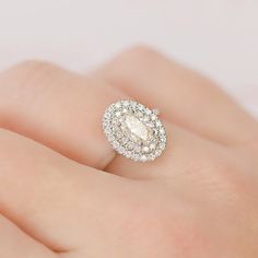 a woman's hand with a diamond ring on top of her finger and an oval shaped diamond in the middle