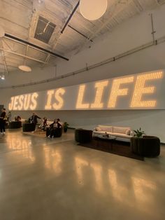 a large sign that says jesus is life in an empty room with people sitting on couches