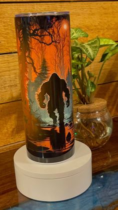 a glass with an image of a person on it sitting on a table next to a potted plant