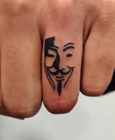 a person's hand with a tattoo that has a mask on the middle finger