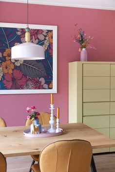 a dining room with pink walls and wooden table surrounded by chairs, vases and flowers