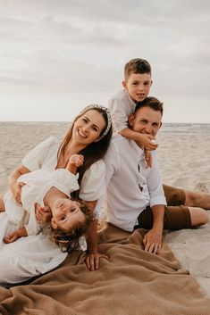 a family is laying on the sand at the beach and posing for a photo together