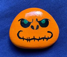 an orange painted pumpkin with green eyes on a blue background, that looks like it has been carved to look like a jack o lantern