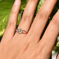 a woman's hand with a ring on it and a plant in the background