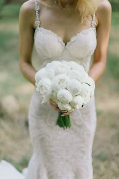 a woman in a wedding dress holding a bouquet of white peonies and roses