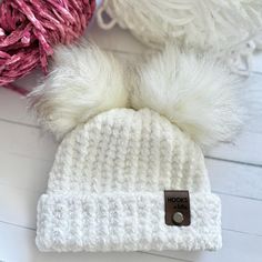 a white knitted hat with two pom - poms next to yarn balls