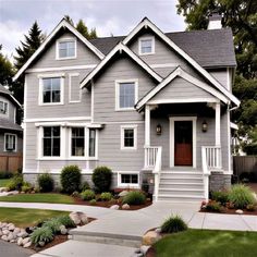 a gray house with white trim on the front door and two story windows, along with landscaping