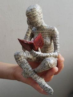 a person is holding a small statue made out of book pages with a red object in their hand