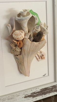 a white frame with shells and seashells hanging on it's side in front of a wall