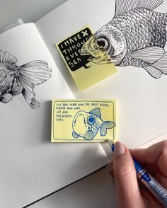 a hand holding a marker next to an open book with drawings on it and a fish stamp