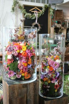 two glass vases filled with flowers sitting on top of a wooden table next to each other