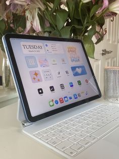 an open laptop computer sitting on top of a white desk next to a vase with flowers