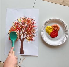 a person holding a green spoon next to a paper plate with a painting on it