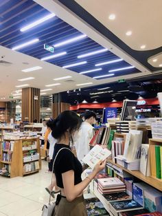 a woman is looking at books in a book store while another person stands behind her