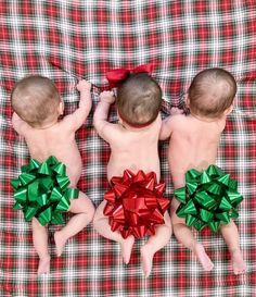 three babies laying on top of a plaid blanket with green and red bows around their backs