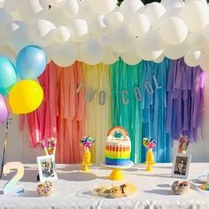 a table topped with lots of balloons next to a rainbow colored cake and desserts