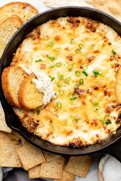 a skillet filled with cheese and crackers on top of a table next to chips