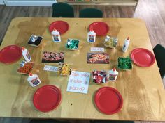 a wooden table topped with red plates covered in pizza and condiments on top of it