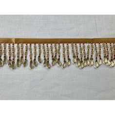 gold and red beaded trim on white fabric with silver metal hooks hanging from it's side