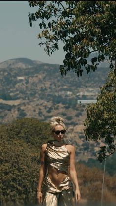 a woman in a gold dress walking down the street with her shirt draped over her shoulders