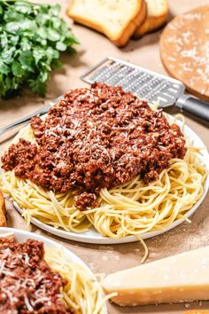 spaghetti with meat sauce and parmesan cheese on a plate next to bread slices