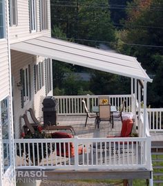 a white porch with chairs and tables on the back deck overlooking an outdoor dining area