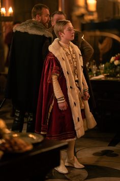 a young boy dressed in medieval clothing standing next to another man wearing a fur coat