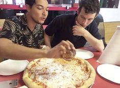 two men sitting at a table eating pizza