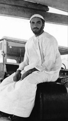 an old photo of a man sitting on a chair with his legs crossed and wearing a white outfit