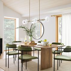 a dining room table with green chairs and a round mirror on the wall above it