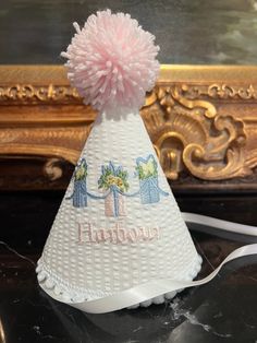 a white hat with pink pom - pom on it sitting on a table