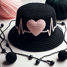 a crocheted hat with a heart on it and balls of yarn in the background