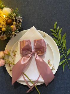 two pink bows are tied on a plate with flowers and greenery in the background