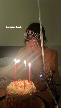 a woman covering her face while sitting in front of a cake with candles on it