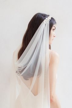 a woman wearing a white veil with flowers on her head is standing in front of a wall