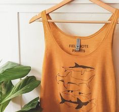 an orange tank top hanging on a wooden hanger next to a green potted plant